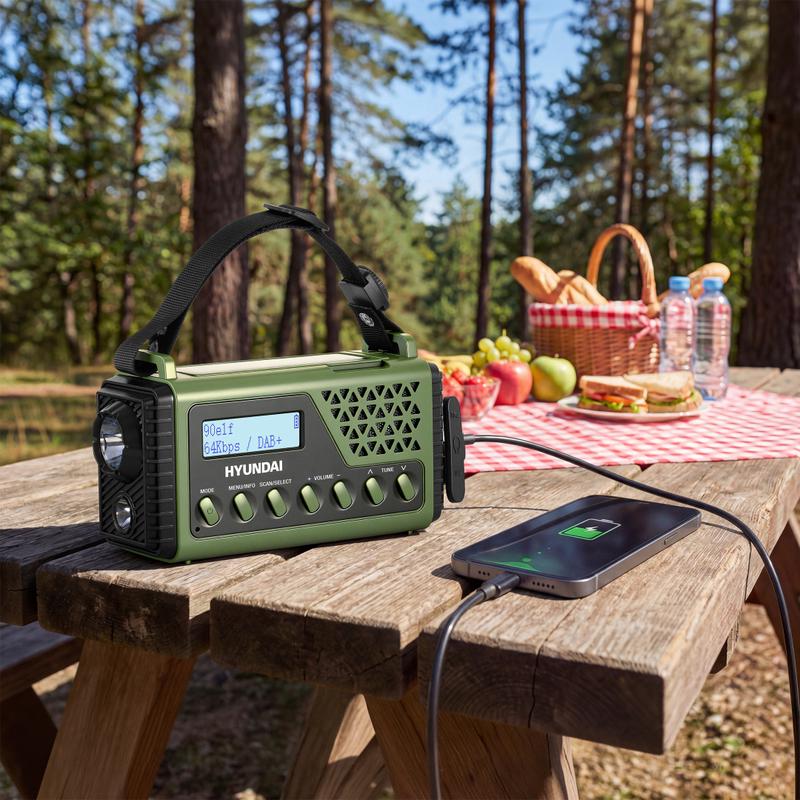 Groene Hyundai noodradio van Action op een picknicktafel die via een kabel een telefoon oplaadt Groene Hyundai noodradio van Action op een picknicktafel die via een kabel een telefoon oplaadt